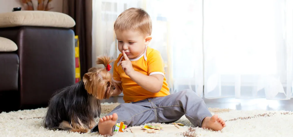 A toddler plays with a small dog on a soft rug