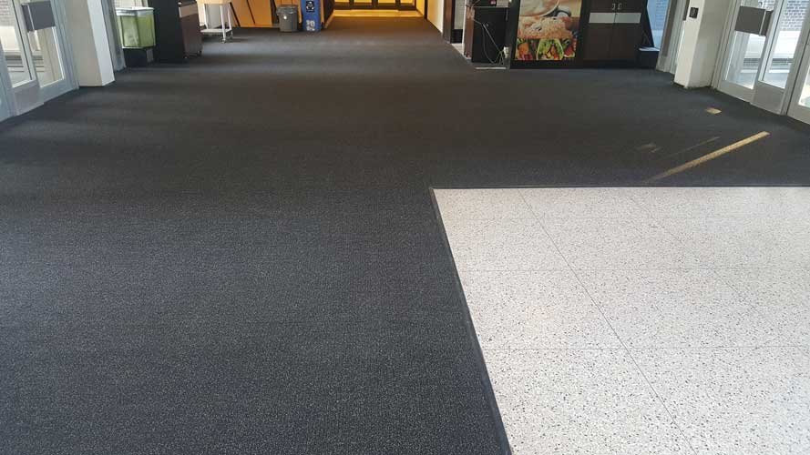 A large dark entrance mat on a pale stone floor inside a building