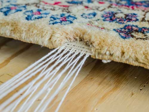 Close-up of the end of a patterned rug, where the white fringe threads leave the pile