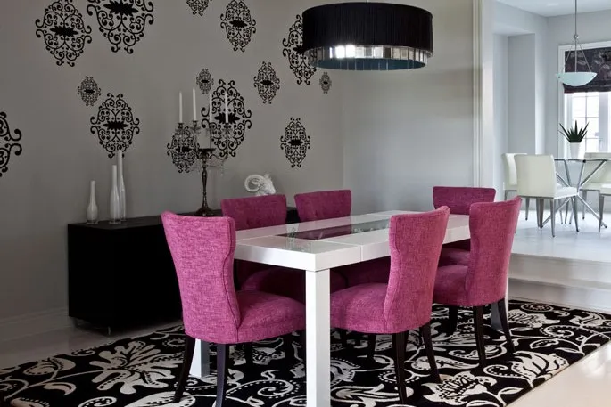 A black and white patterned rug under a white dining table with pink chairs