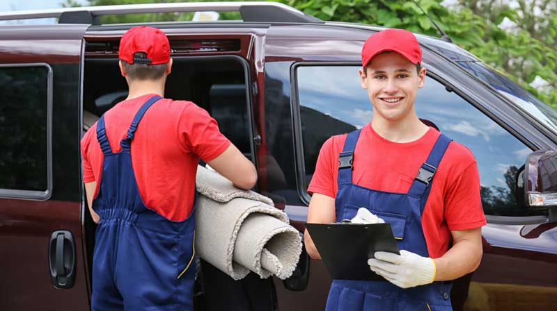 Two movers carry rolled-up rugs to their van