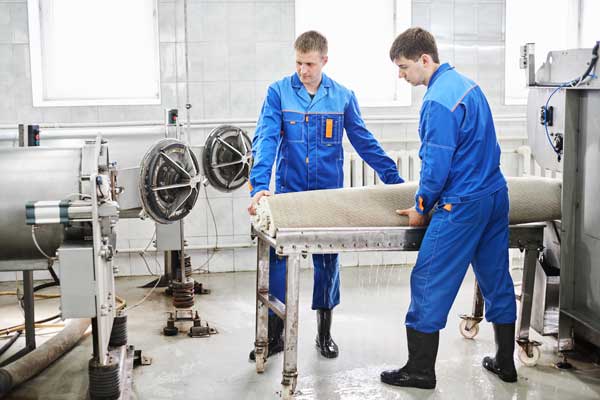 Two workers carry a rolled-up rug between them