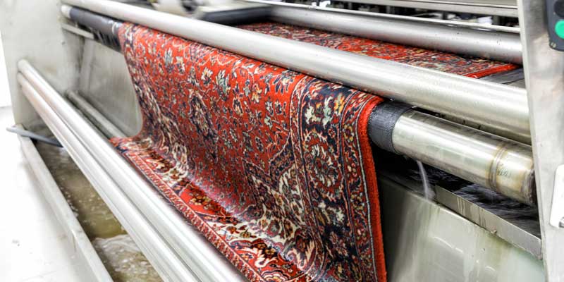 A red oriental rug moving through washing rollers at a rug cleaning facility