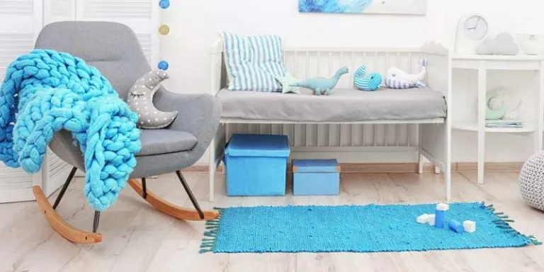 A bright blue cotton rug beside a white crib in a nursery