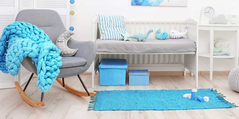 A bright blue cotton rug on the floor of a nursery, beside a crib and a rocking chair