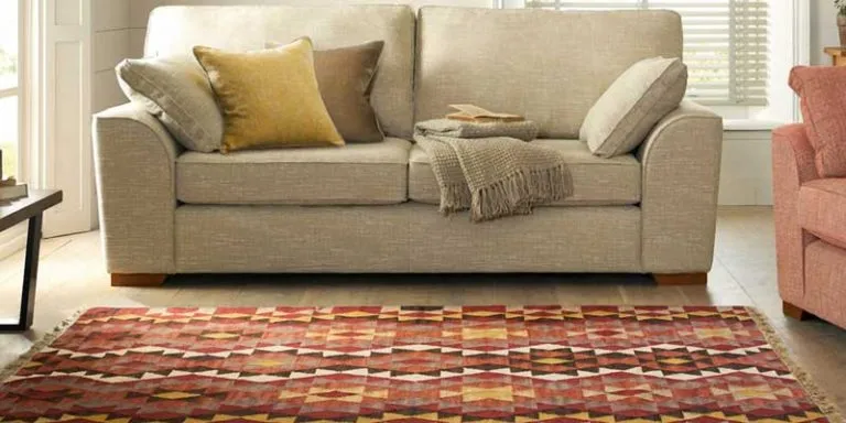 A red diamond-pattern flat-weave rug in front of a beige sofa