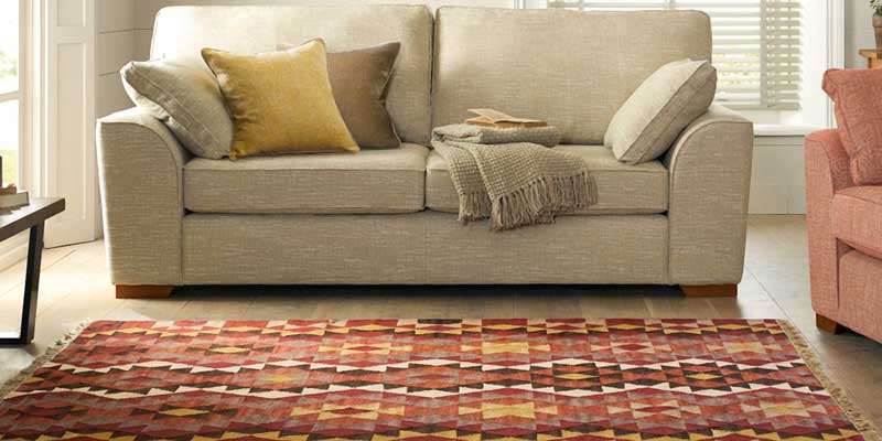 A red, orange and cream flat-weave rug with a diamond pattern in front of a beige sofa