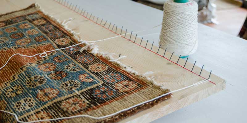 A rug on a work table with a spool of thread for edge binding
