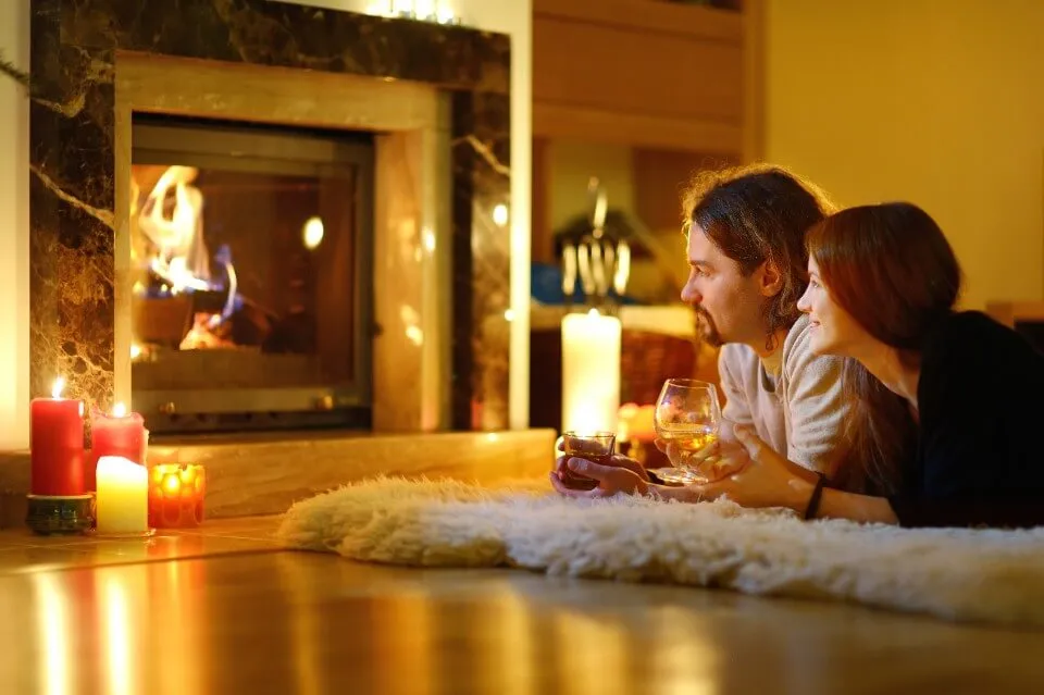 A couple relax on a soft white rug in front of a warm fireplace