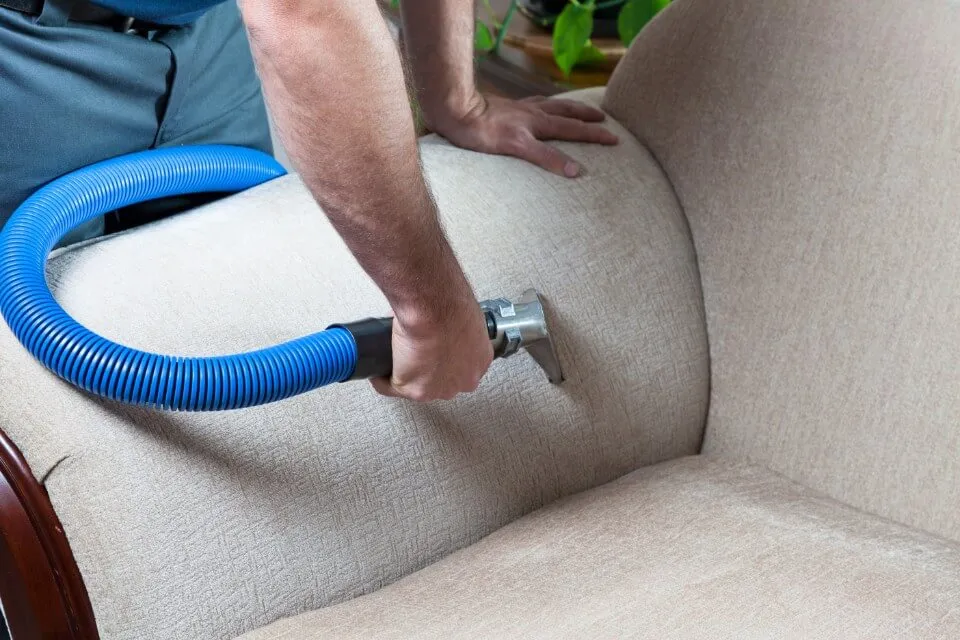 A fabric sofa being cleaned with an upholstery tool