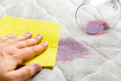 A hand blots a red wine spill with a yellow cloth