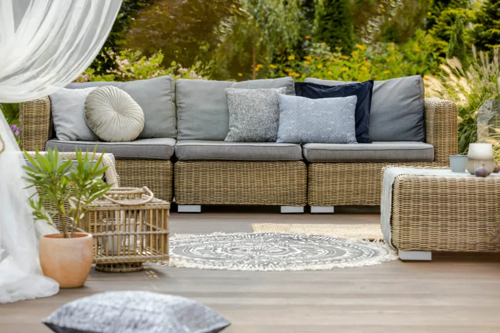 A round woven outdoor rug on a wooden deck in front of a wicker patio sofa