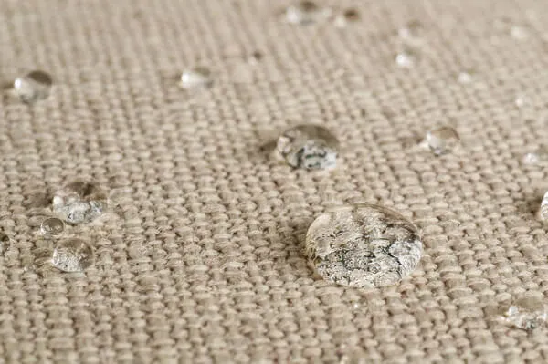 Close-up of round water drops resting on a woven beige fabric